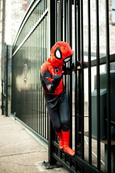 a person in a spiderman costume leans against a gate