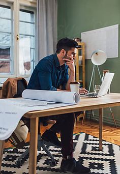 a man sitting at a desk with a laptop and papers in front of him, talking on the phone