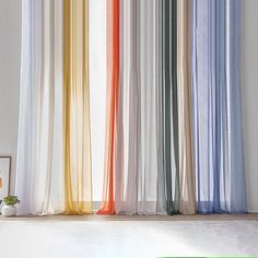 an open window with multicolored curtains and a potted plant on the floor