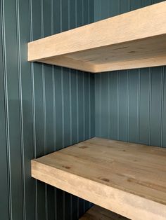 two wooden shelves in the corner of a room with green walls and wood flooring