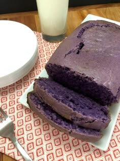 a loaf of purple cake sitting on top of a white plate next to a glass of milk