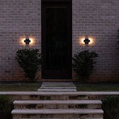 two lights are lit up on the side of a brick building with steps leading to it