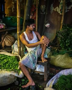 a man sitting on top of a wooden bench next to bags of vegetables and herbs