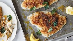 three fish fillets on a baking sheet with lemon wedges and parmesan cheese