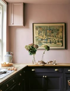 a kitchen with pink walls and black cabinets is pictured in this image, there are two vases on the window sill