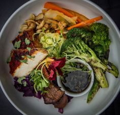 a white plate topped with meat and veggies next to dipping sauce on top of it