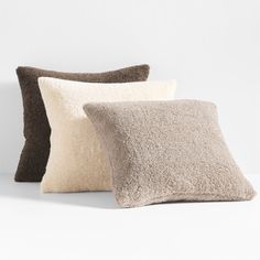 three pillows sitting next to each other on top of a white surface with one brown and one beige pillow