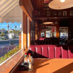 the inside of a restaurant with red booths and tables in front of large windows looking out onto an empty street