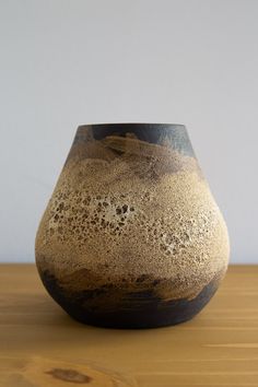 a brown and black vase sitting on top of a wooden table