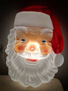 a lighted santa claus head with blue eyes and beard, wearing a red christmas hat