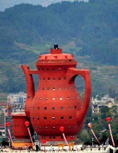 a large red vase sitting in the middle of a body of water next to a city