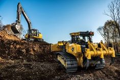 two yellow bulldozers are parked in the dirt