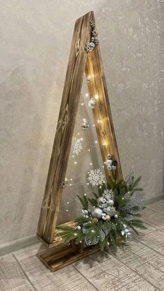 a wooden christmas tree with lights and ornaments in it on the floor next to a wall