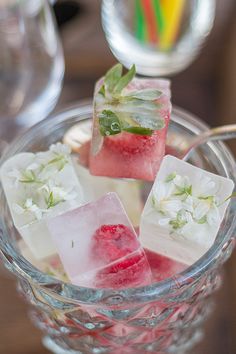 some ice cubes with strawberries and flowers on them in a glass bowl next to two wine glasses