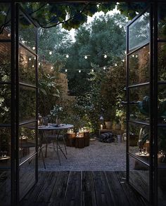 an open door leading to a patio with lights hanging from the ceiling and trees in the background