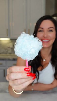 a woman holding a cotton candy lollipop in her right hand and smiling at the camera