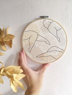 a hand is holding up a cross - stitch pattern on a white wall next to some yellow leaves