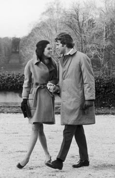 a man and woman are walking together in the snow, one is wearing a trench coat