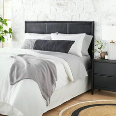 a bed with white sheets and pillows next to a night stand in front of a brick wall