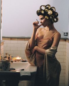 a woman in a bathrobe brushing her teeth while sitting on a bathroom sink