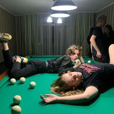 two people laying on top of a pool table with balls in front of them and one person reaching for the ball