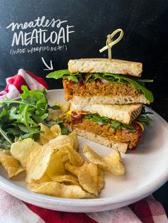 a white plate topped with a sandwich and chips next to a chalkboard sign that says meatloaf