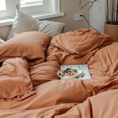 an unmade bed with brown sheets, pillows and a book on the floor next to it