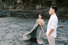 a man standing next to a woman in a dress on top of a sandy beach