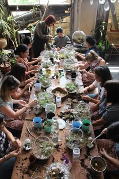 a group of people sitting around a wooden table with plates and bowls filled with plants