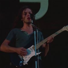 a man with long hair playing an electric guitar in front of a microphone on stage