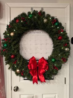 a christmas wreath is hung on the front door with a red bow and green ornaments