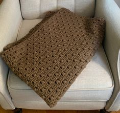 a brown crocheted blanket sitting on top of a white chair