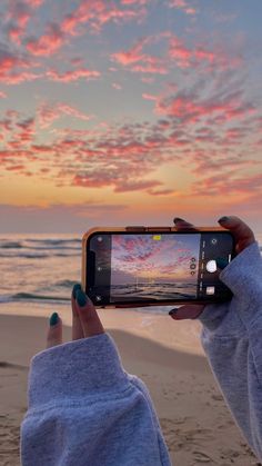 a person taking a photo with their cell phone on the beach at sunset or sunrise