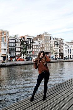 a woman standing on top of a wooden pier next to the water with buildings in the background