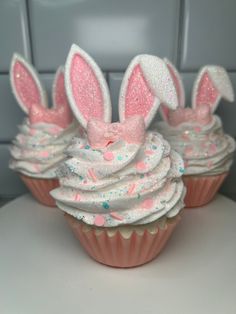 three cupcakes decorated with bunny ears and pink frosting on a white table