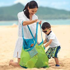 a woman and child on the beach with a green mesh bag in front of them