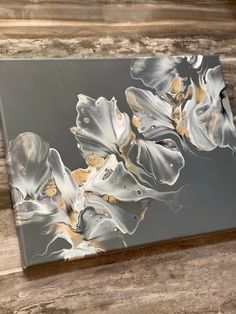 an abstract painting is displayed on a wooden surface with white and gold flowers in the center