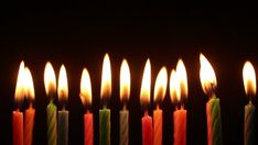 many lit candles are lined up in a row on a black background, with one glowing orange and the other green