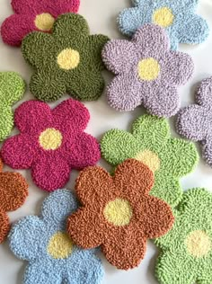 crocheted flowers are laid out on a white surface with green, blue, pink, and yellow petals