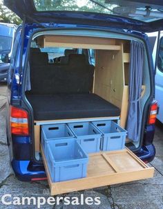 the back end of a blue van with its doors open and several storage bins in it