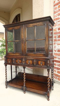 an old wooden cabinet with glass doors on the top and bottom, in front of a brick wall