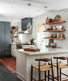 a large kitchen with lots of counter space and wooden shelves on the wall, along with two bar stools