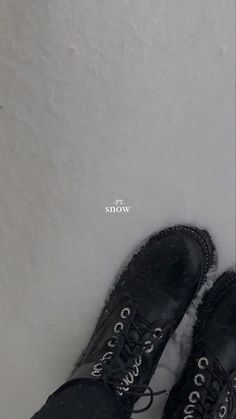 a pair of black shoes sitting on top of snow covered ground next to a white wall