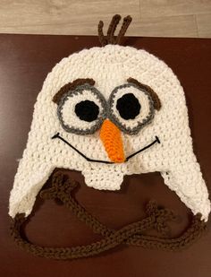 a crocheted hat with an orange nose and large eyes on top of a brown table