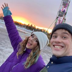 a man and woman standing next to each other in front of a ferris wheel at sunset