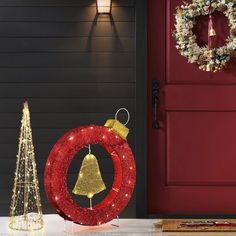 a red door with a christmas wreath and a gold bell on it next to a tree