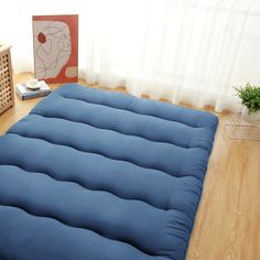 a blue futon mattress sitting on top of a wooden floor next to a window