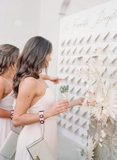 two women standing next to each other in front of a wall with flowers on it