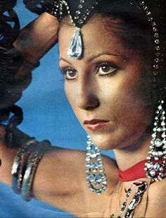 a woman with jewelry on her head and hands behind her head, in front of a blue background