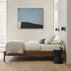 a white bed sitting next to a window in a bedroom on top of a wooden floor